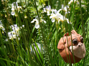 Zarte Irisblüten hinter Allium Knospen und Keramikvogel.